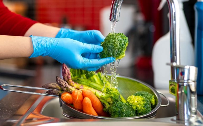 Woman washing vegetables on kitchen counter.